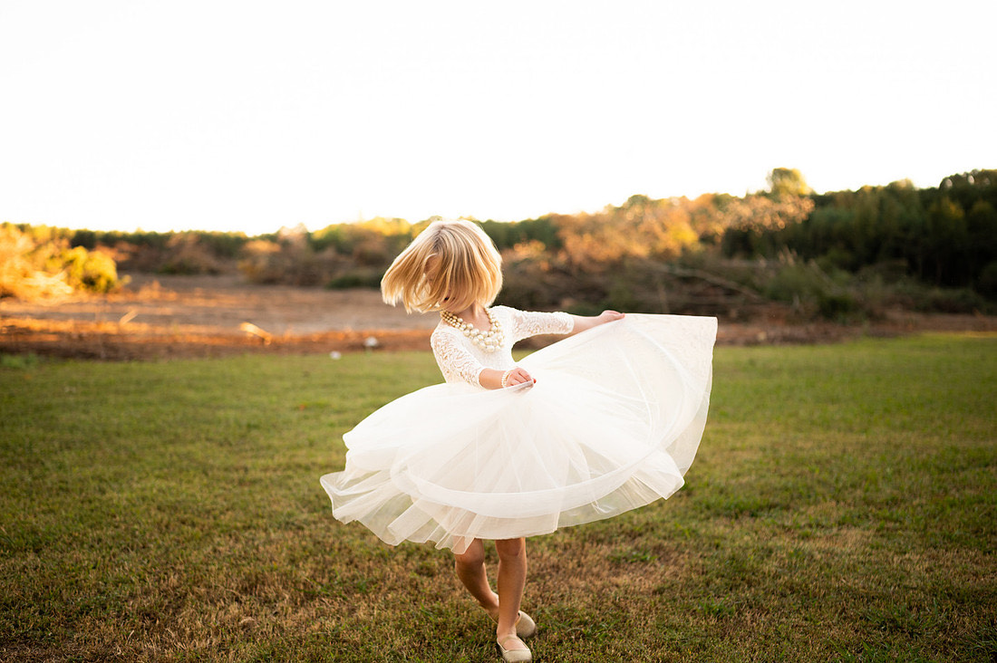 Young child twirling in a white dress at sunset