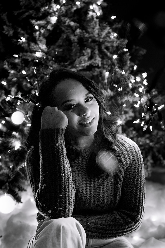 Young woman seated beside glowing Christmas lights in black and white