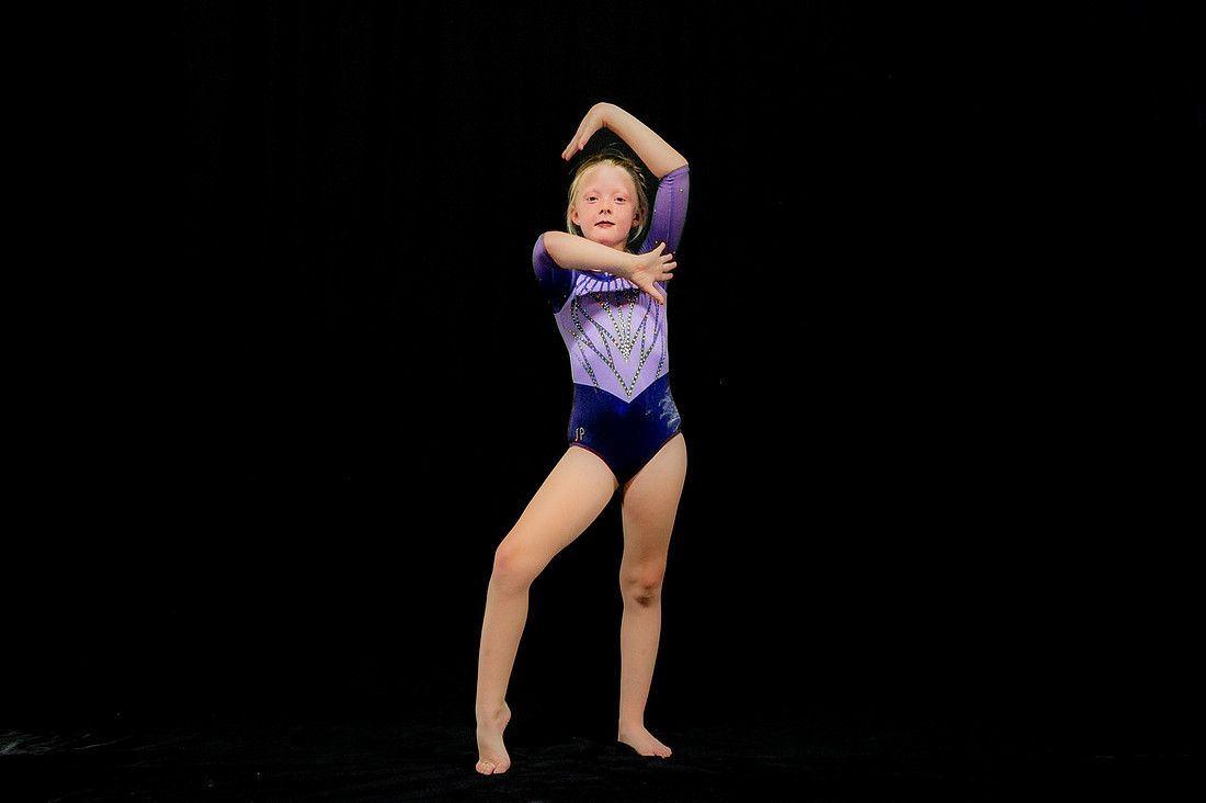Young gymnast posing against a black backdrop