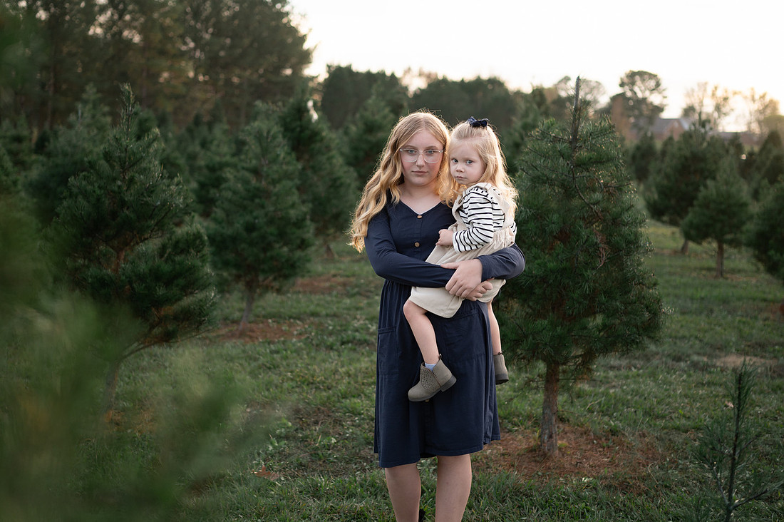 Older sister holding a younger child in an evergreen field